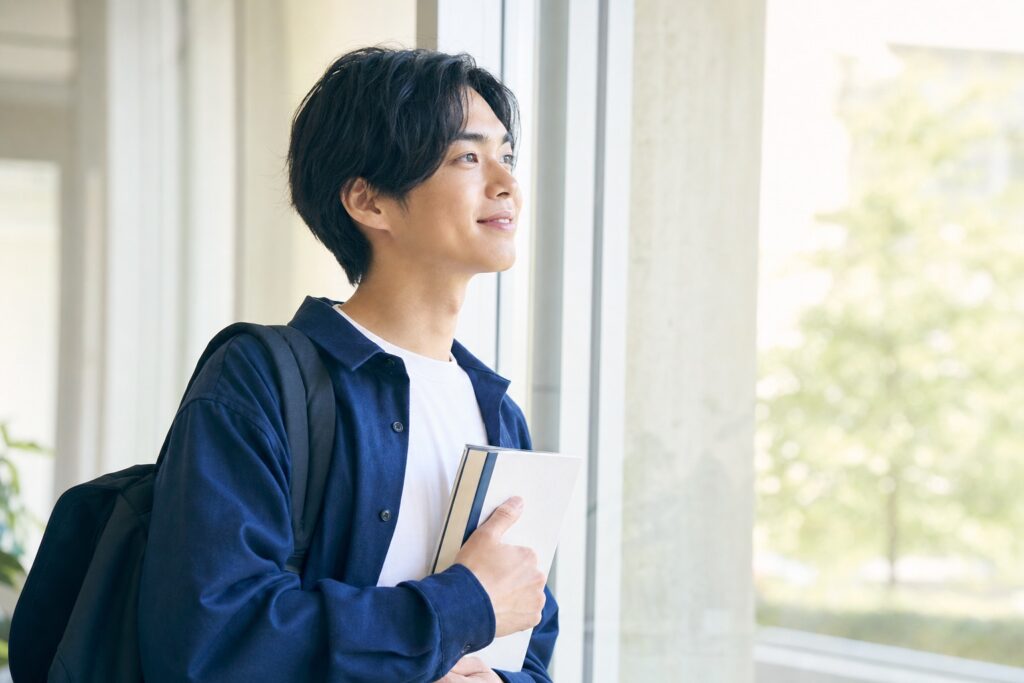 窓辺で安堵の表情を浮かべる男子学生